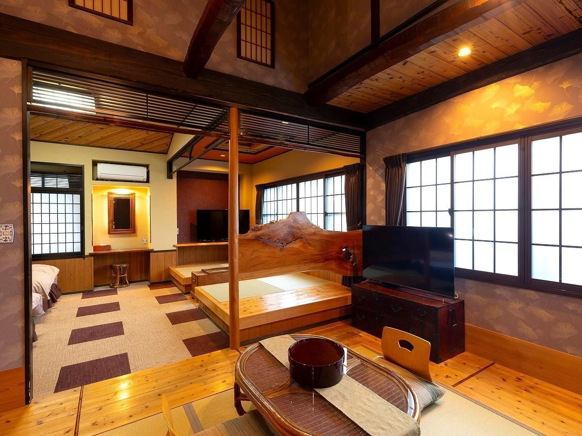 Una habitación tradicional japonesa con suelo de tatami, una cama de madera baja, un televisor y una puerta corrediza que da a otra habitación.