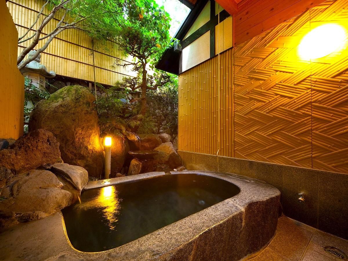 Un onsen japonés tradicional con una bañera de piedra rodeada de rocas y una pared de bambú.