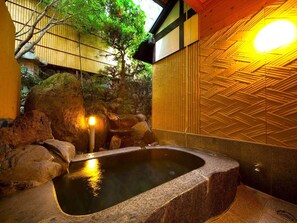 Een traditioneel Japans onsen met een stenen bad omringd door rotsen en een bamboe wand.