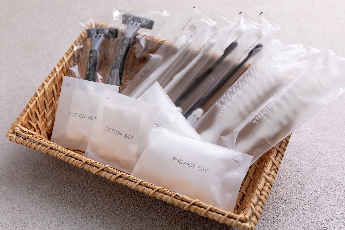 Ein Korbwäscher mit mehreren Plastiktüten, die Artikel mit den Aufschriften 'COTTON SET' und 'SHOWER CAP' enthalten.