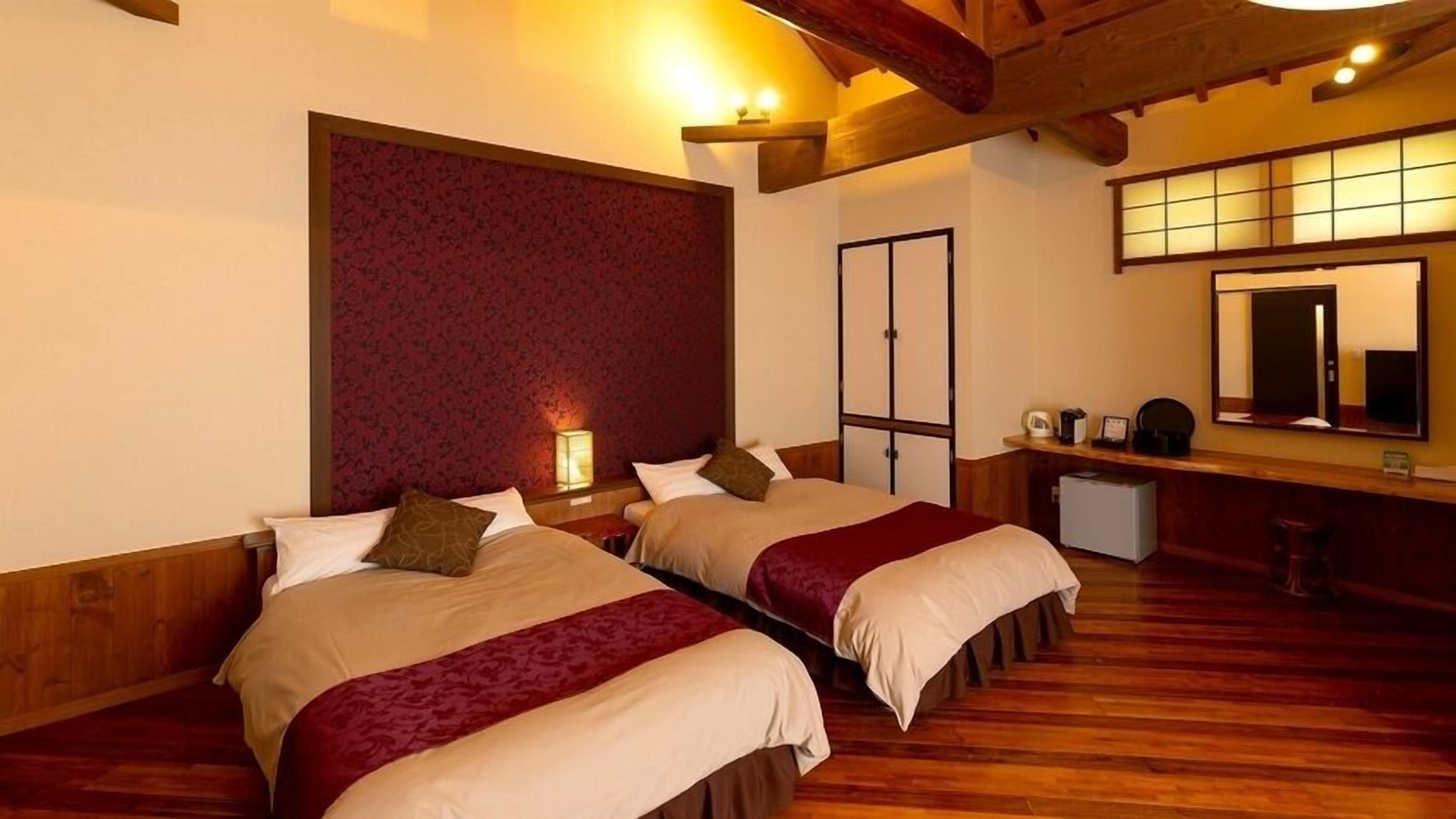 Habitación de hotel con dos camas, suelo de madera, un espejo grande y un escritorio pequeño con una silla.