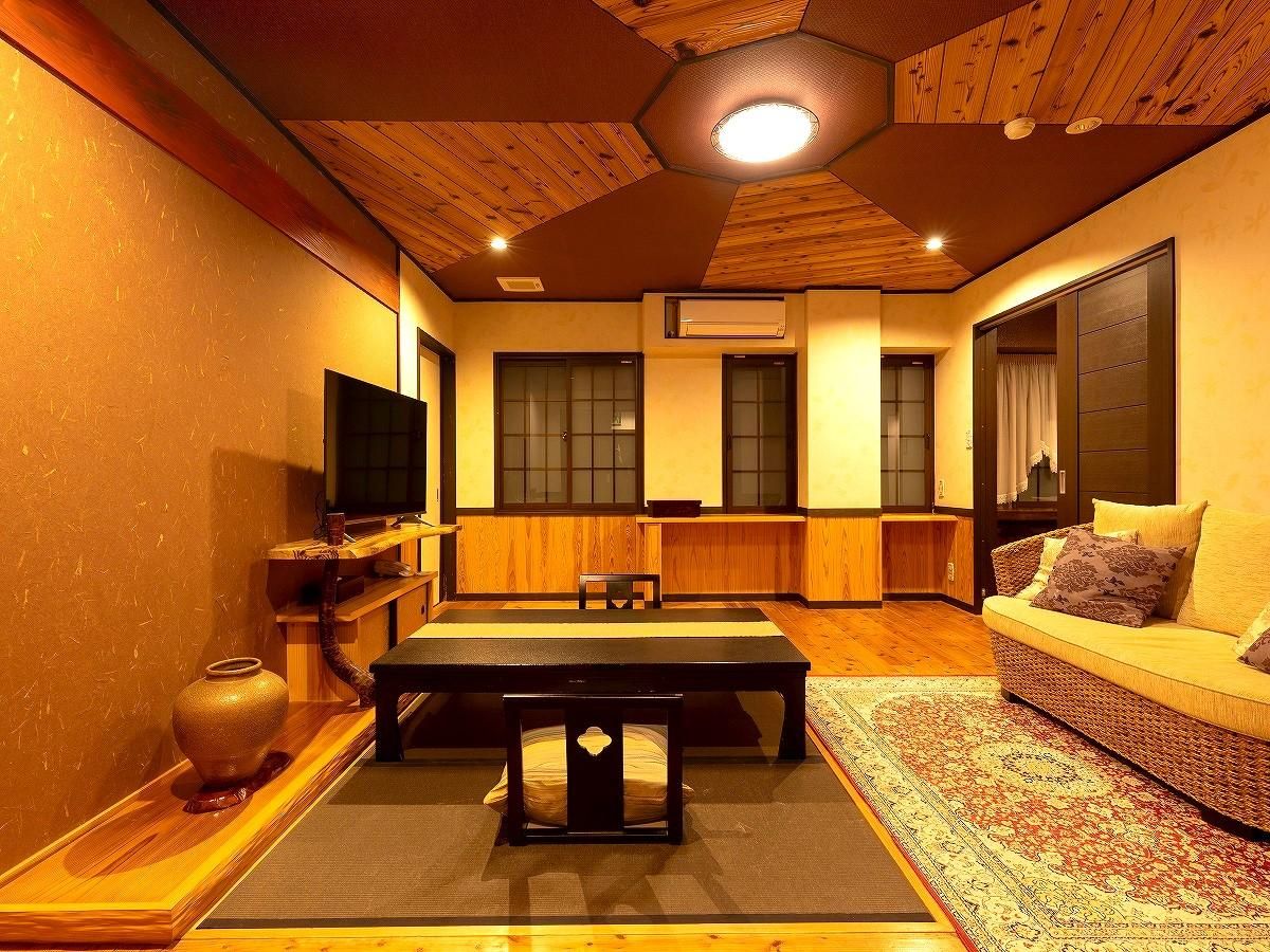 Una habitación tradicional japonesa con suelo de tatami, una mesa baja, un sofá y un ventanal grande.