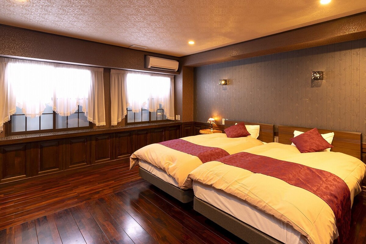 A double bed with two pillows, a bedside table with a lamp, and a window with curtains.