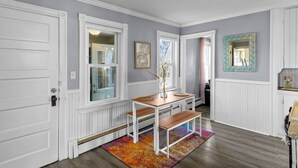 Un couloir avec des portes blanches, un banc en bois, une petite table sur laquelle est posé un vase, et un tapis coloré.