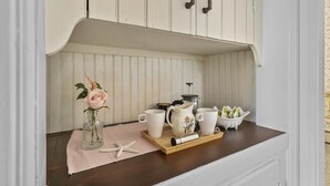 Un comptoir de cuisine avec une machine à café, un pichet et des tasses disposés sur un plateau en bois.