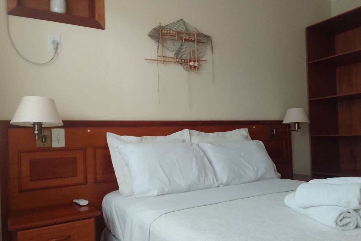 A neatly made bed with white linens, a wooden headboard, and two bedside lamps.