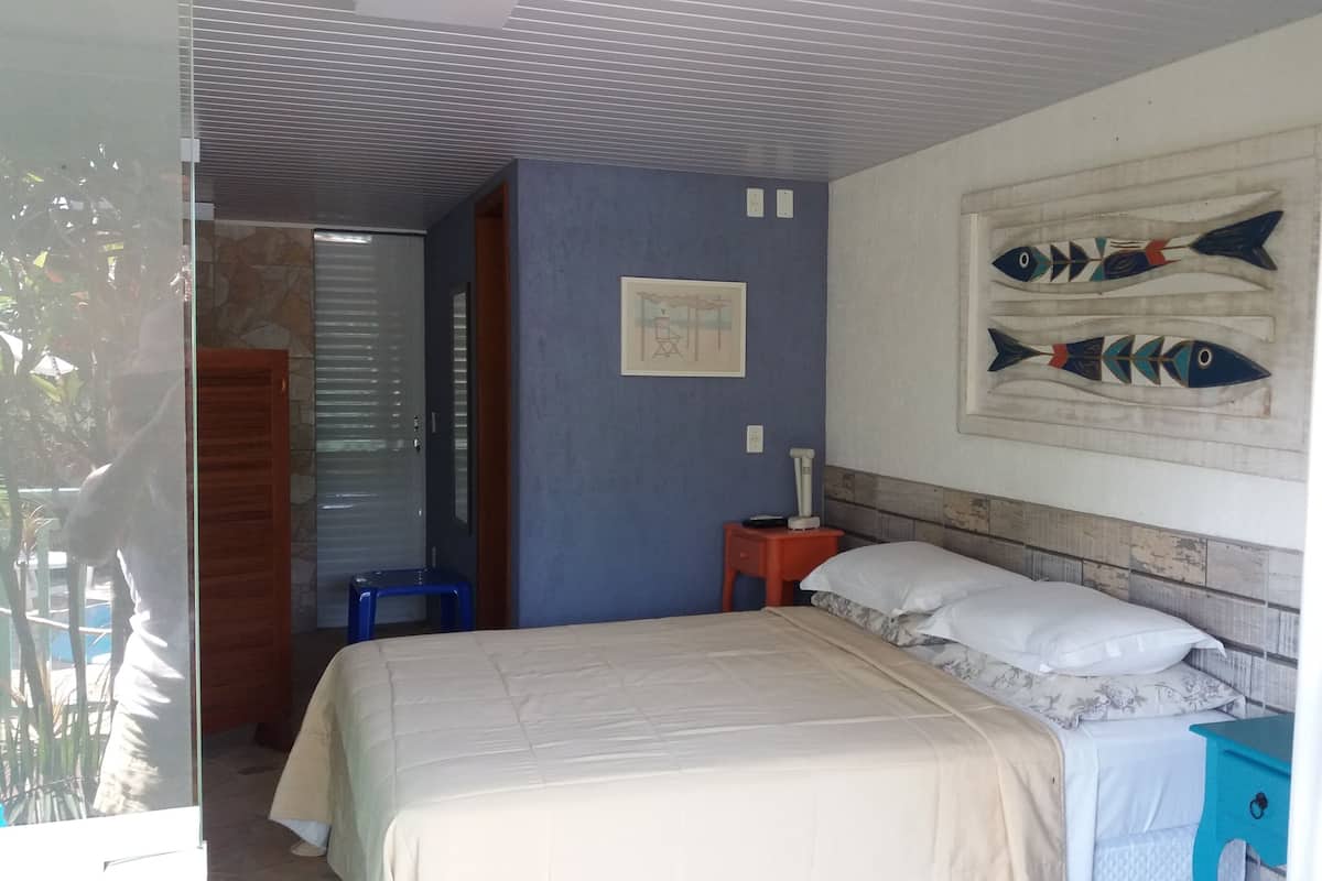 A bedroom with a bed, a nightstand, a wall-mounted fish decoration, a blue stool, and a door leading to another room.