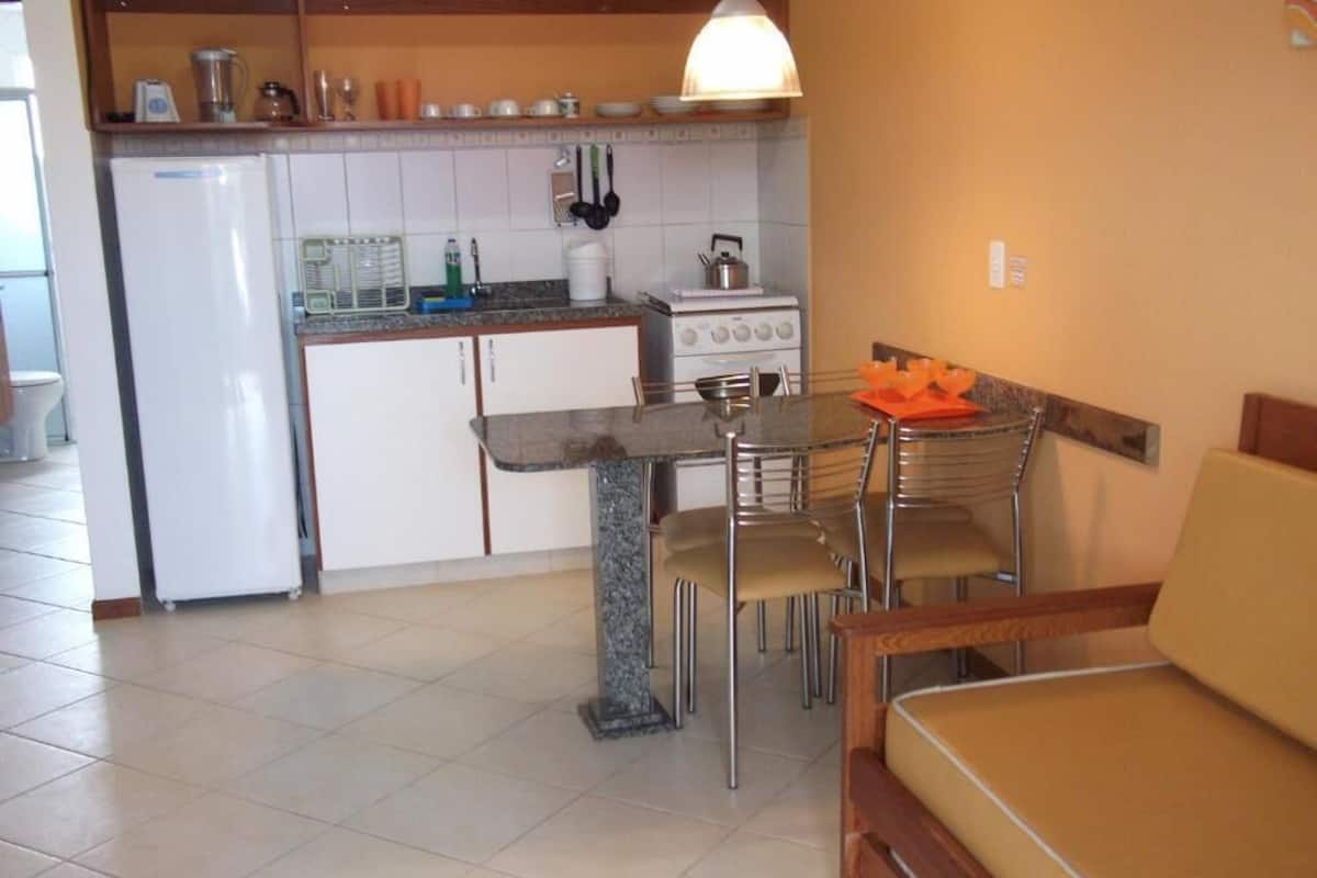 A compact kitchen with a refrigerator, stove, and dining area with chairs and a table.