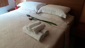 Una cama bien hecha con sábanas blancas, una toalla enrollada y una sola flor.