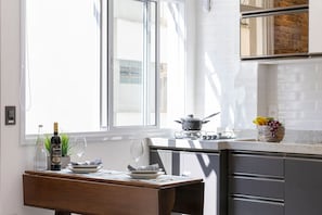 Uma cozinha com uma mesa de jantar, uma garrafa de vinho, uma taça de vinho e uma cesta de frutas.
