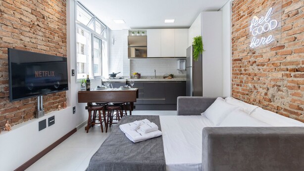 Ein modernes Hotelzimmer mit Backsteinwand, Flachbildfernseher, Sofa, Essbereich und Küche.