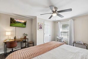 Une chambre d’hôtel équipée d’un lit, d’un bureau, d’une chaise, d’un ventilateur de plafond, d’une télévision et d’une fenêtre avec des rideaux.