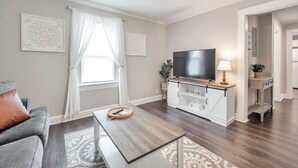 A modern living room with a flat-screen TV, a ceiling fan, and a dining area with a wooden table. - Cute Modern Townhouse Close to MTSU, Parks & Downtown: Large Master & Coffee Bar (Murfreesboro)
