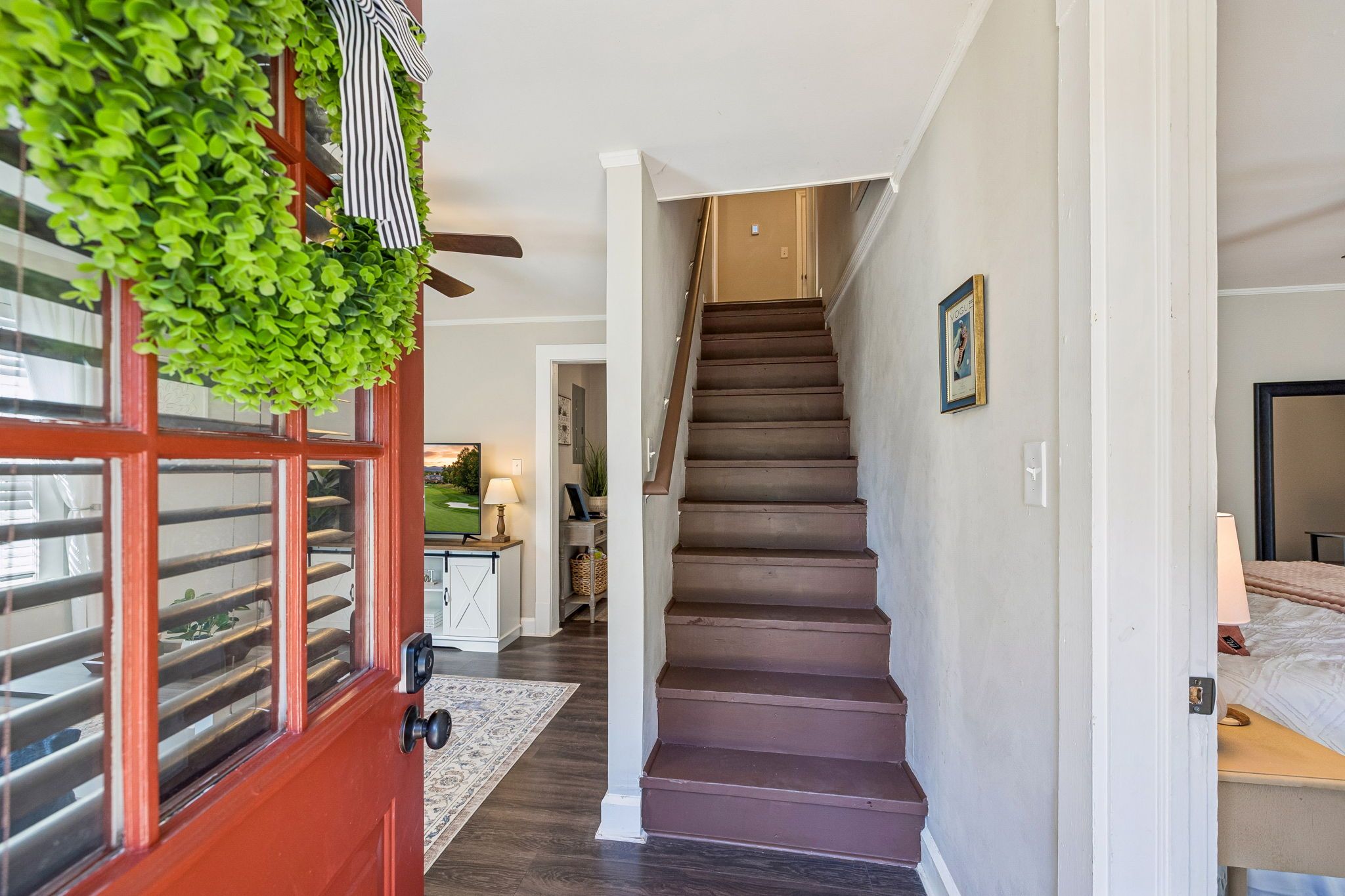 A staircase leading to a second floor, a red door with a window, and a hallway with a rug.