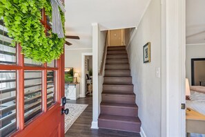 Un escalier menant à un deuxième étage, une porte rouge avec une fenêtre et un couloir agrémenté d’un tapis.
