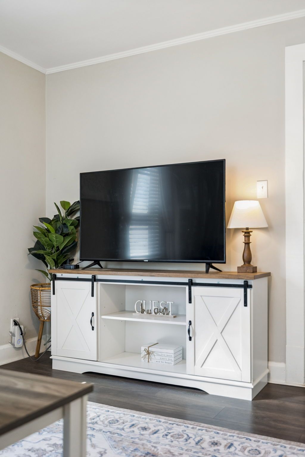 A flat-screen TV mounted on a white cabinet with a plant beside it.