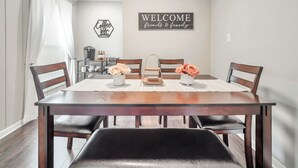 A dining area with a wooden table, chairs, a coffee station, and a welcome sign. - Cute Modern Townhouse Close to MTSU, Parks & Downtown: Large Master & Coffee Bar (Murfreesboro)