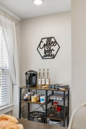A coffee bar setup with a coffee maker, sugar, cream, and coffee mugs on a shelf.