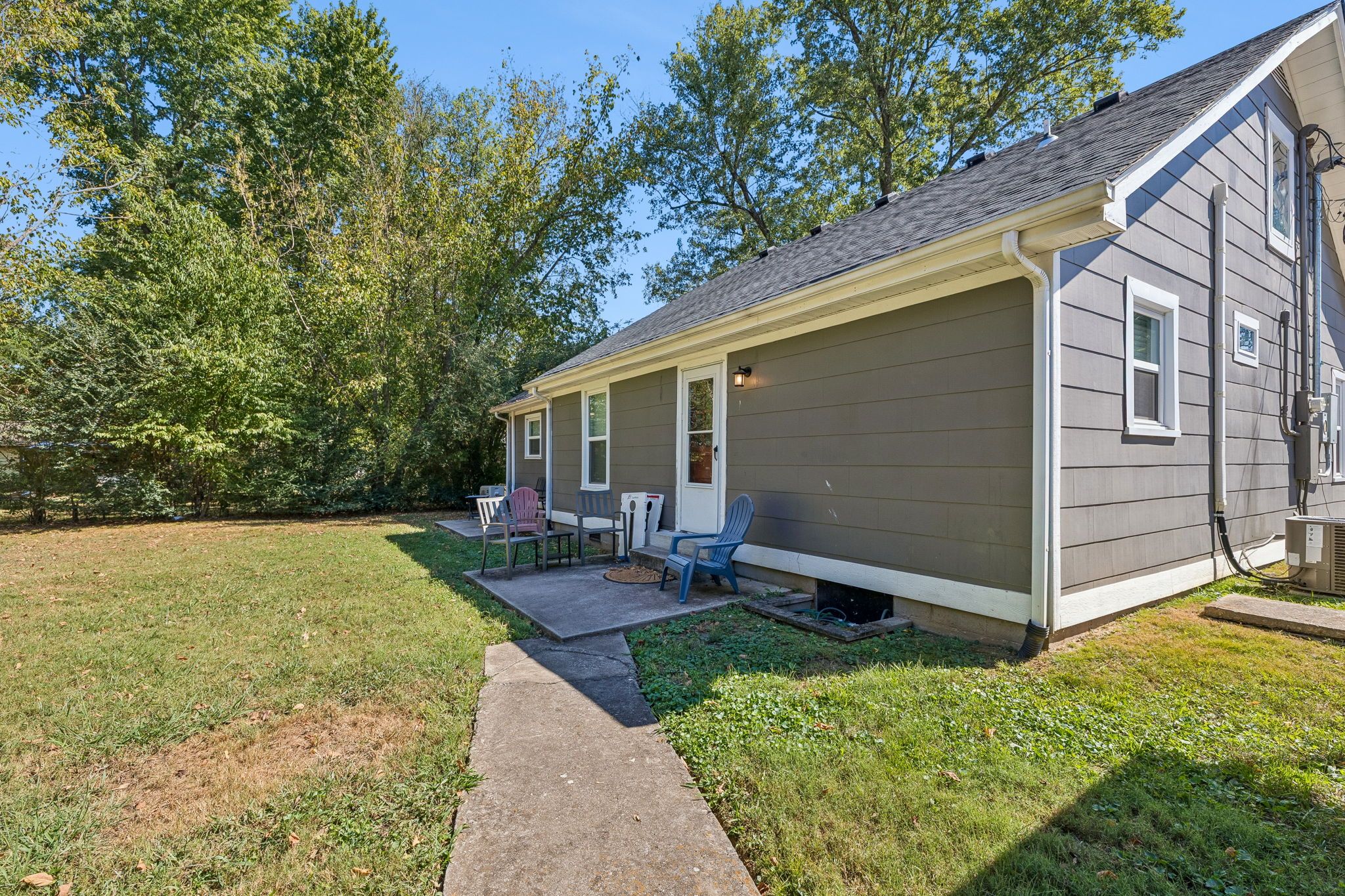 A residential building with a covered patio area, outdoor seating, and a pathway leading to the entrance.