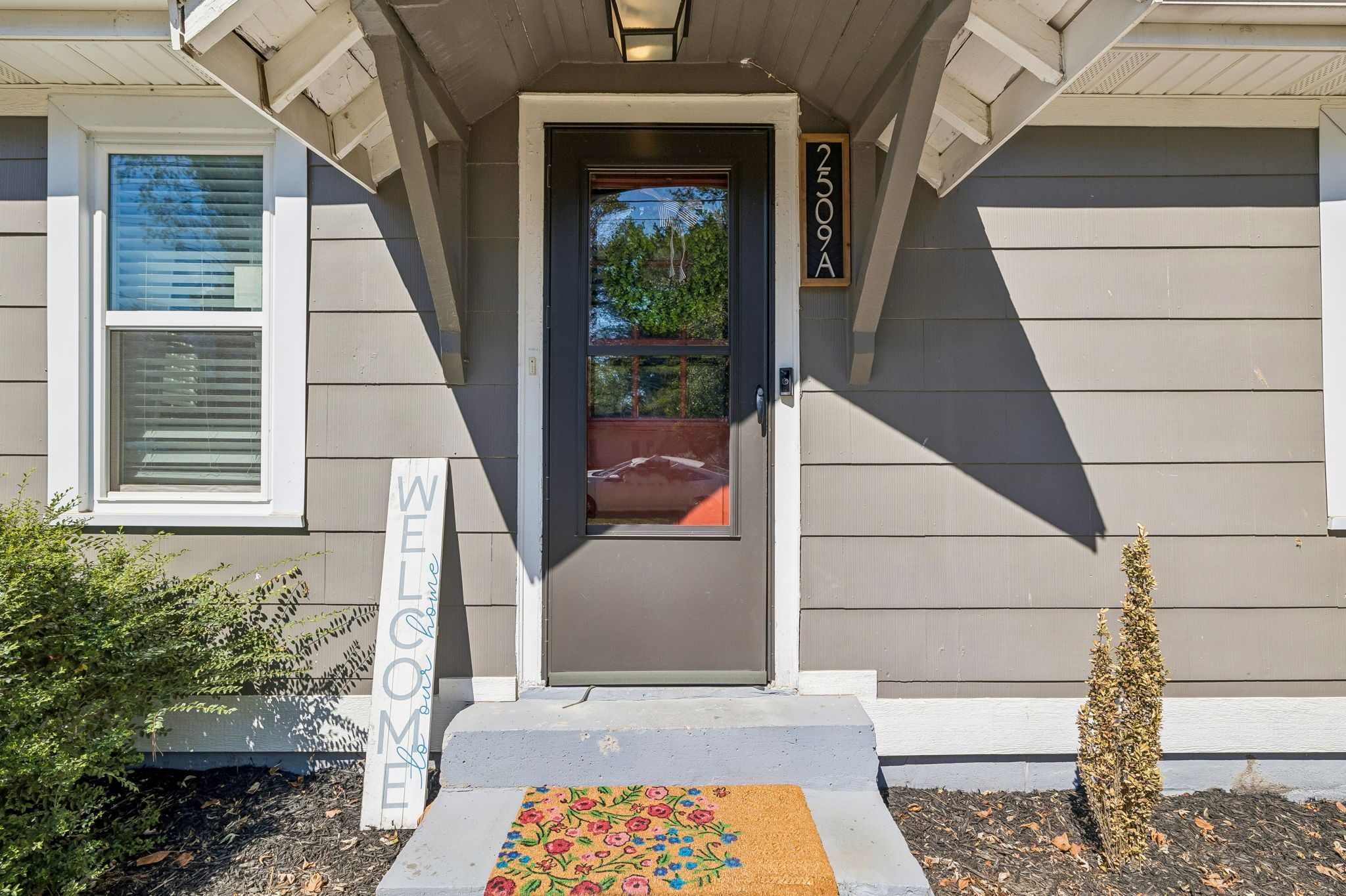A house entrance with a welcome mat, a mailbox, and a number sign.