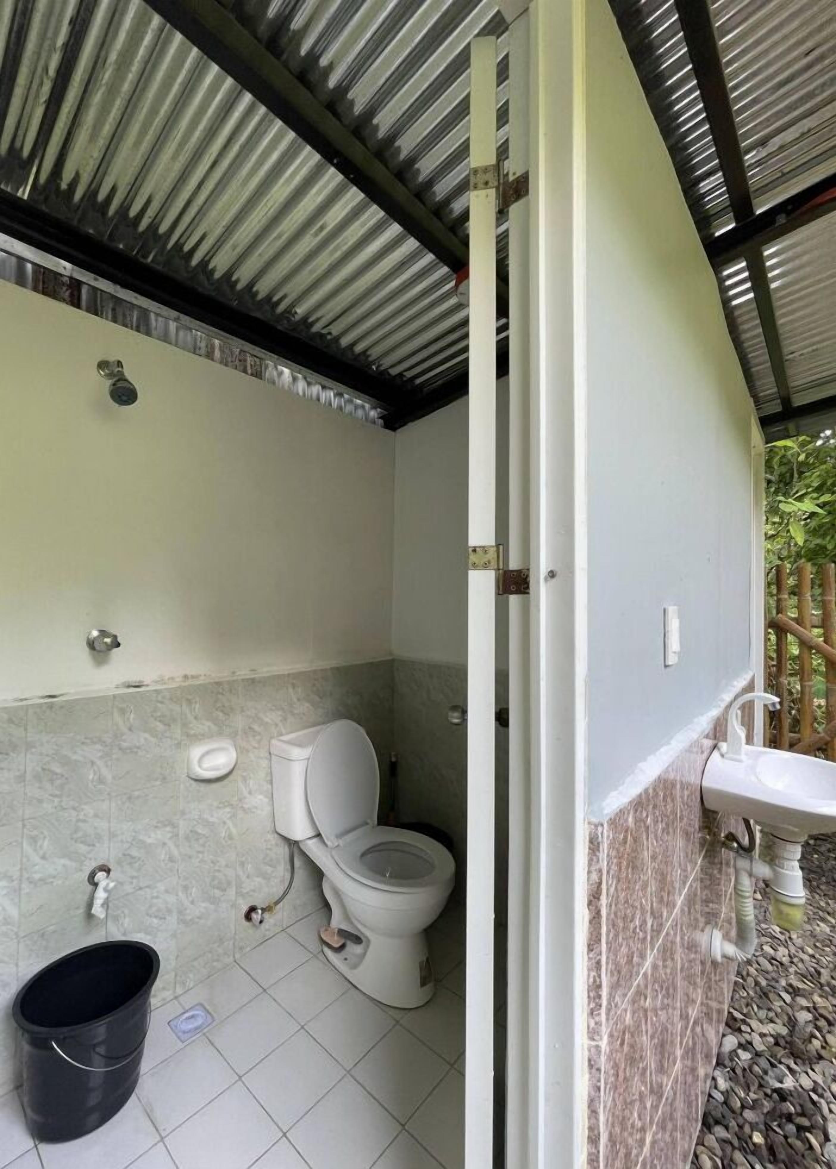 Un bagno con un water, un lavandino e un secchio nero sul pavimento.