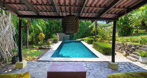 A covered swimming pool with a stone patio, surrounded by lush greenery and a pergola with a patterned ceiling. - Casa Paraiso - Tropical Getaway Close to Beach (Esterillos Oeste)