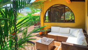 A sunlit patio with a wicker sofa, a small table, and a potted plant. - Casa Paraiso - Tropical Private Pool Near Beach (Esterillos Oeste)