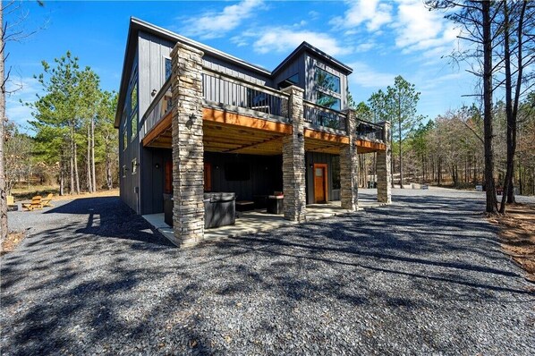 A modern two-story house with a stone facade, large windows, and a covered outdoor area. - Amazing Outdoor Area:  Pool Table, Hot Tub, Close to Attractions!  (Broken Bow)