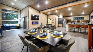 A spacious living area with a dining table set for six, a kitchen with modern appliances, and a large window offering a view of the outdoors. - Amazing Outdoor Area:  Pool Table, Hot Tub, Close to Attractions!  (Broken Bow)