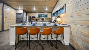 A modern kitchen with a central island, bar stools, and wooden paneling. - Amazing Outdoor Area:  Pool Table, Hot Tub, Close to Attractions!  (Broken Bow)