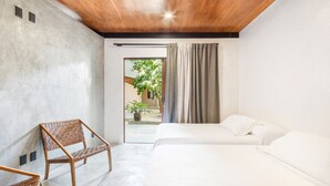 Una camera da letto moderna con soffitto in legno, un letto, una sedia e vista su un giardino attraverso una porta aperta.