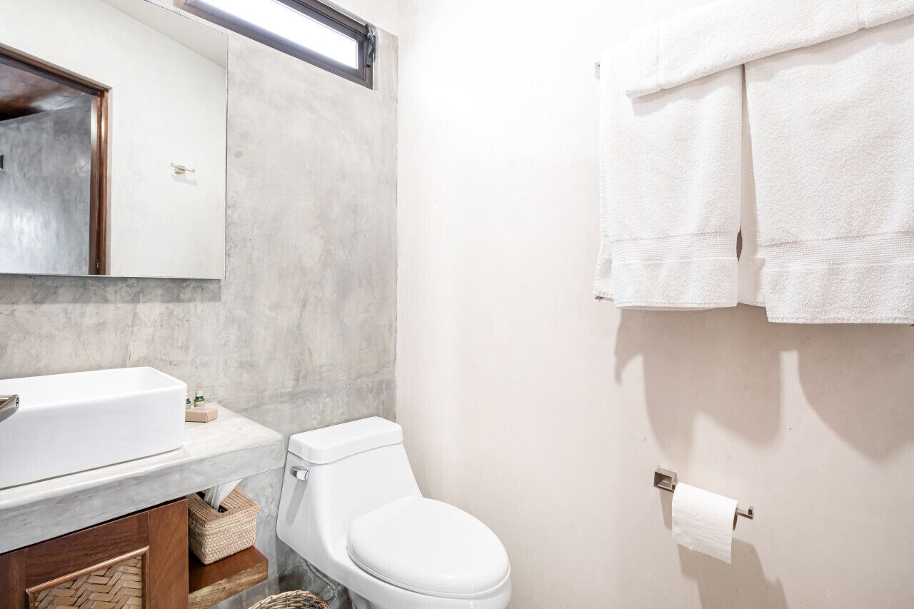 A bathroom with a white sink, mirror, and toilet. There are towels hanging on the wall and a toilet paper holder.