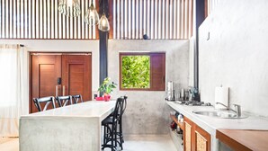 Una cocina moderna con una isla central, taburetes de bar, una ventana con follaje e iluminación colgante.
