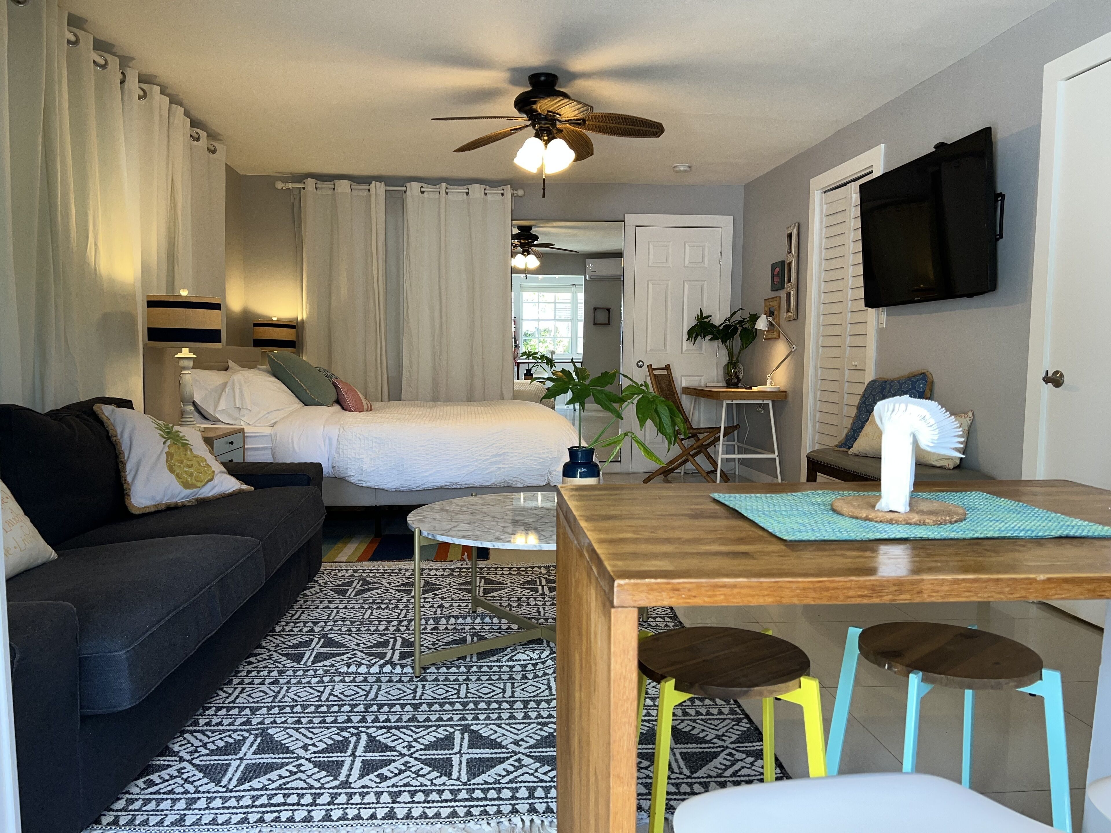 A cozy hotel room with a bed, a sofa, a dining table, and a ceiling fan.