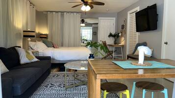 A cozy hotel room with a bed, a sofa, a dining table, and a ceiling fan.