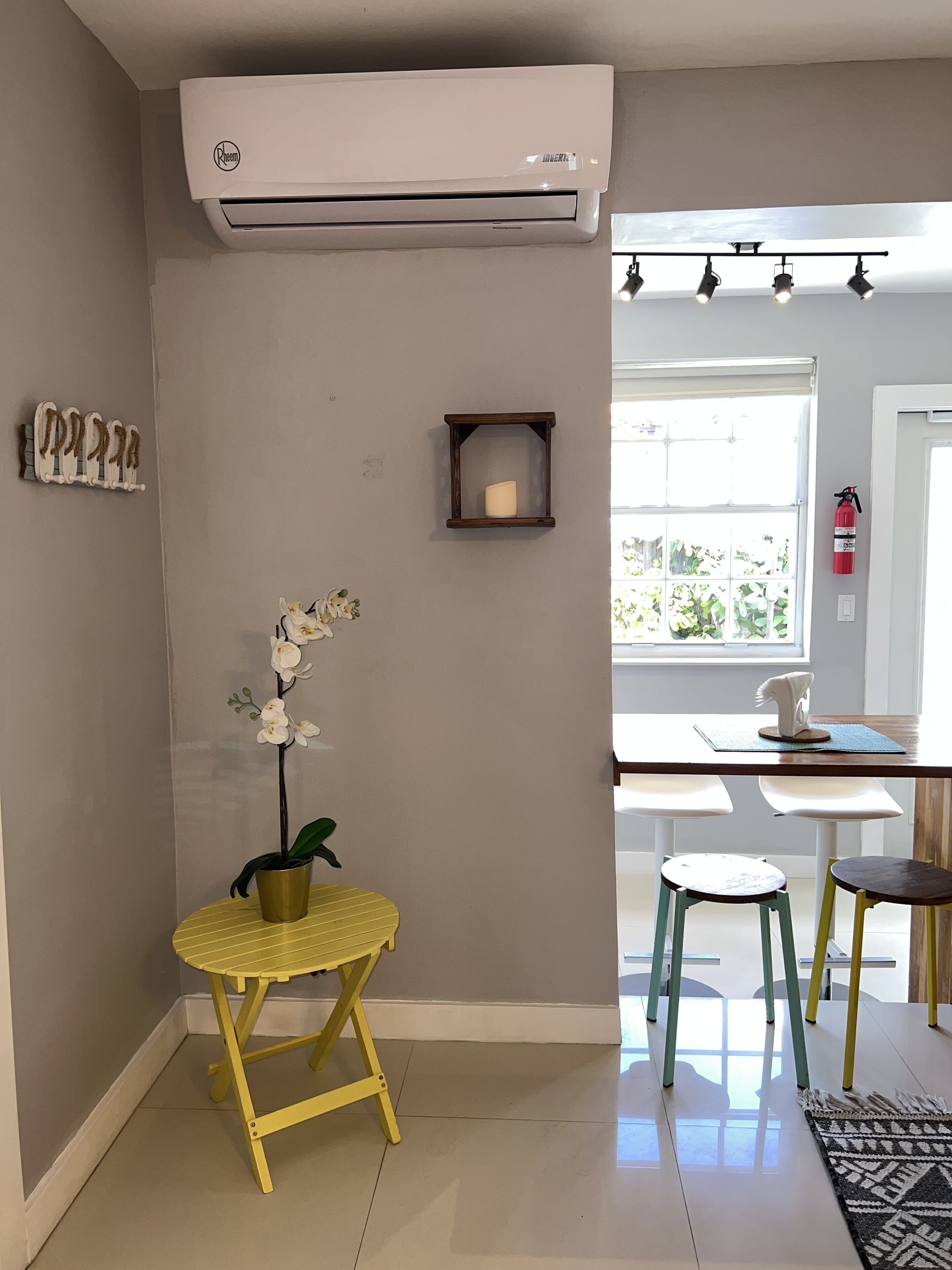 A modern kitchen with a built-in air conditioner, a small potted orchid, a wooden shelf, and a window with a view of greenery.
