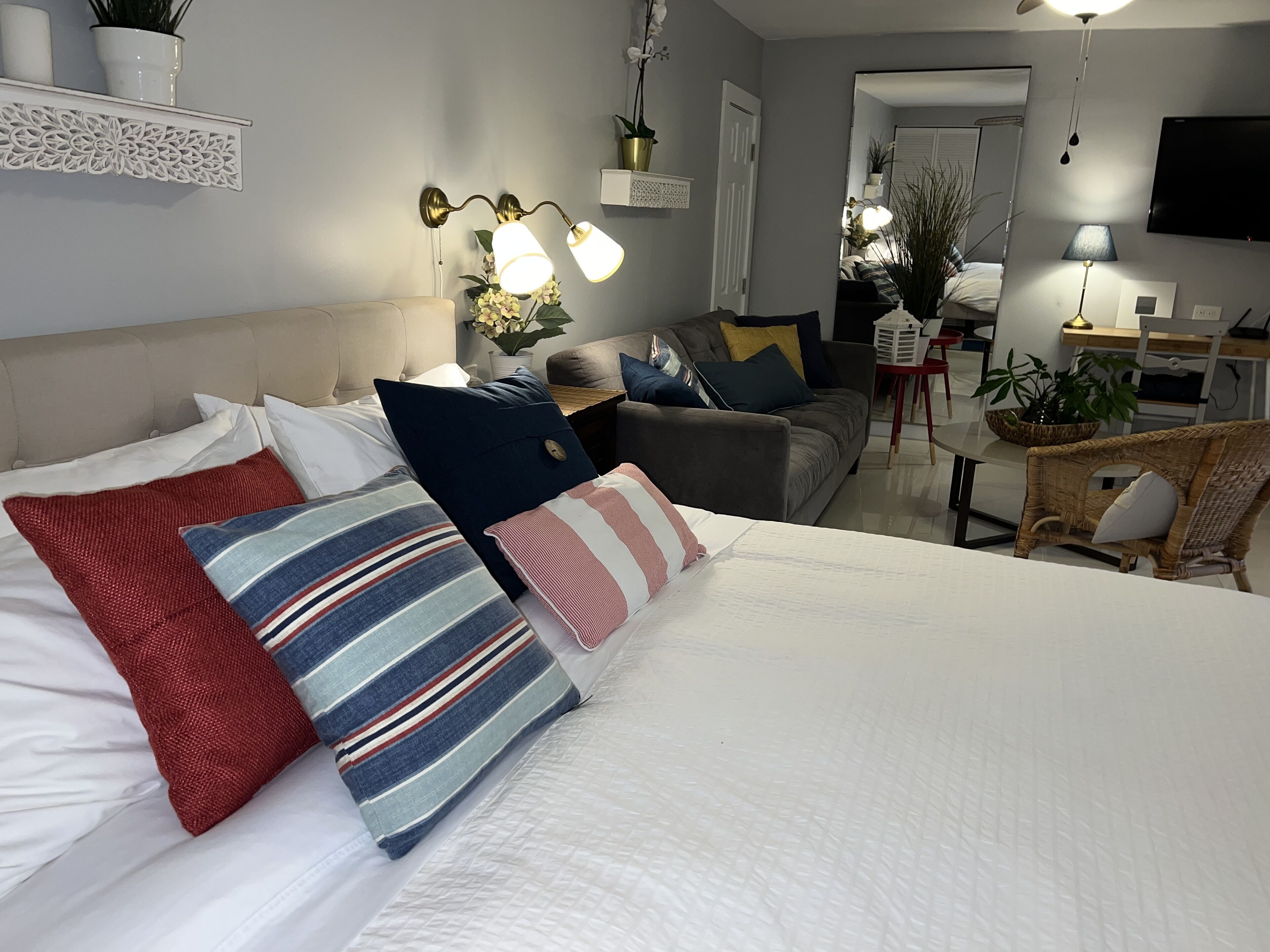 Ein helles Hotelzimmer mit einem großen Bett, einer Couch, einem Esstisch und einem an der Wand montierten Fernseher.