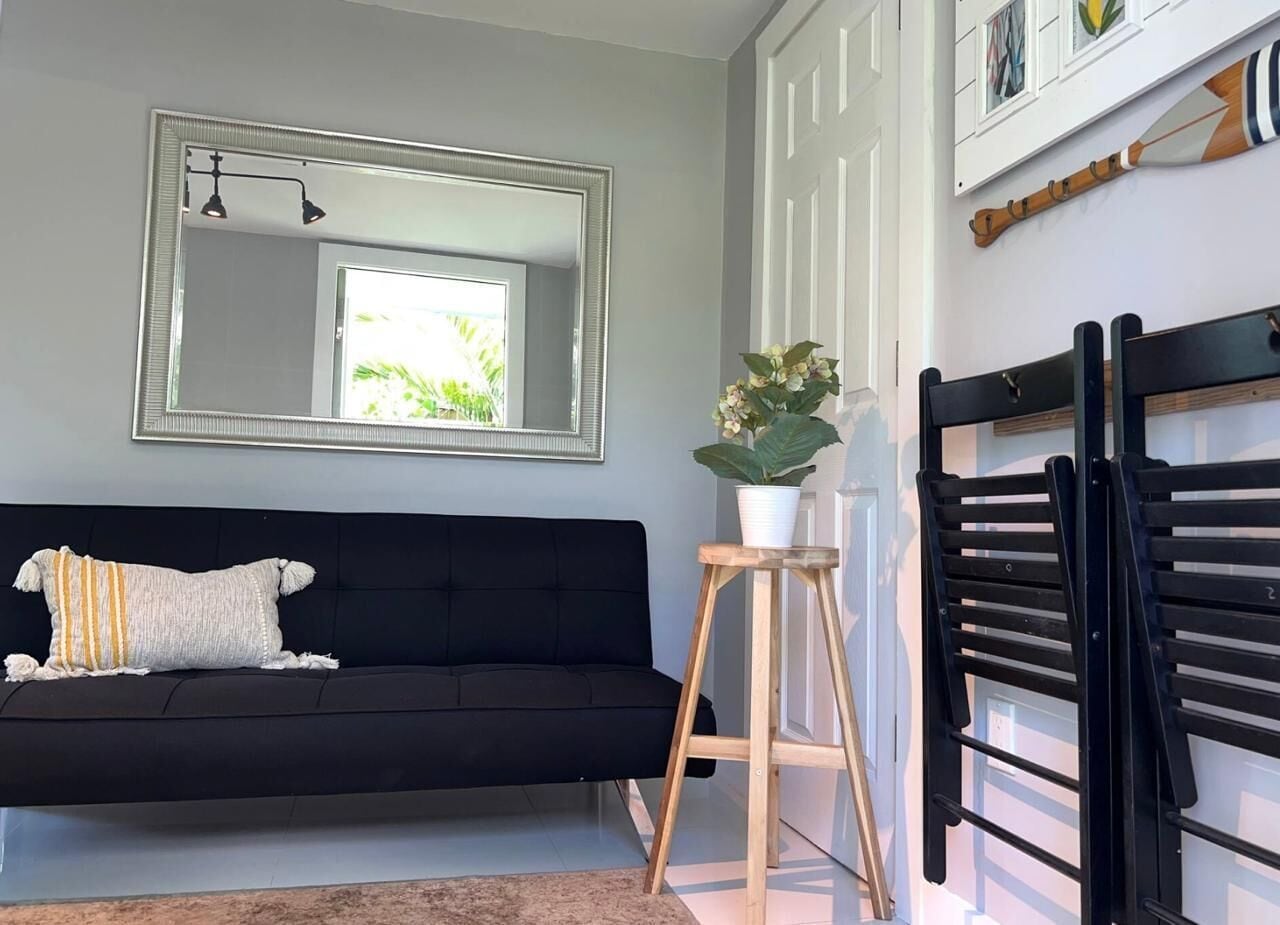 A room with a black sofa, a mirror, a wooden stool with a plant, and a black metal rack.