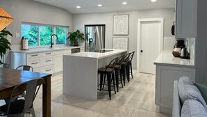 A modern kitchen with a large island, bar stools, and a dining area with a table and chairs.