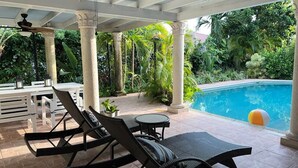 A covered outdoor area with a pool, lounge chairs, and a table.