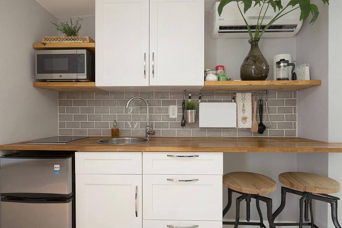 A compact kitchen with white cabinets, a microwave, a refrigerator, a sink, and a wooden countertop.