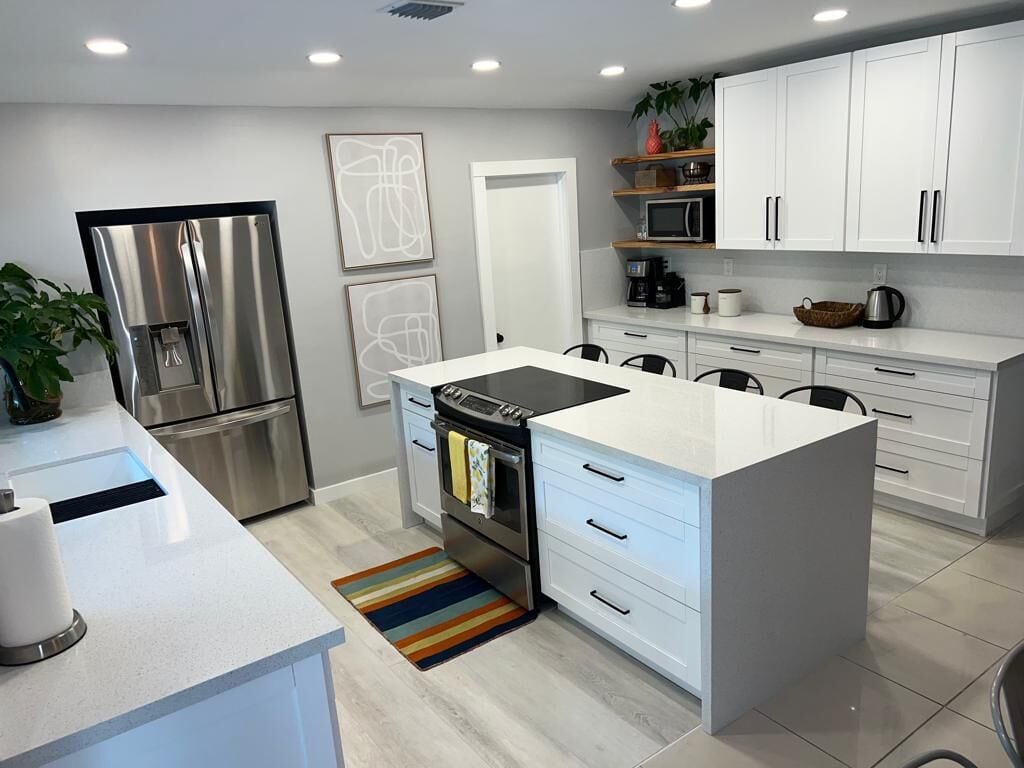 Uma cozinha moderna com armários brancos, eletrodomésticos de aço inoxidável e uma ilha central.