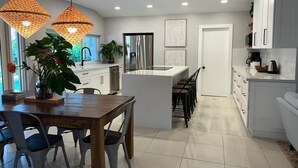A modern kitchen with a central island, pendant lights, and a dining area with chairs.