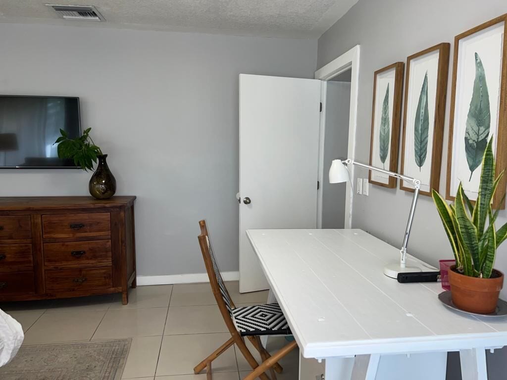A room with a white desk, a chair, a television on the wall, a wooden cabinet, and a door.