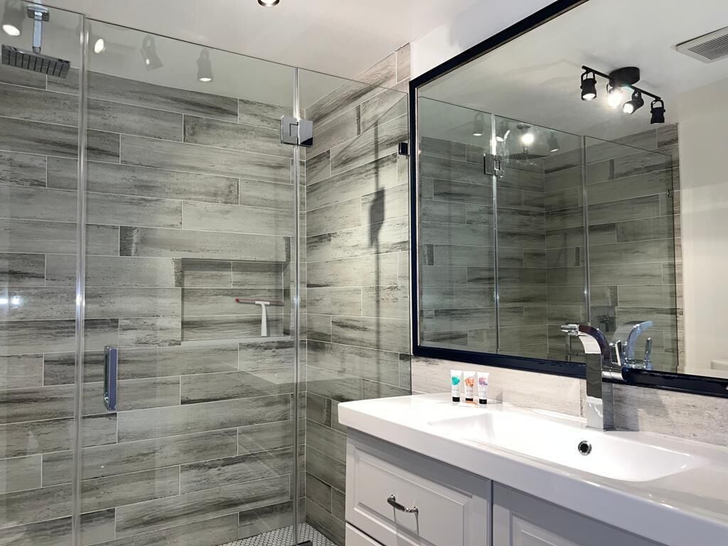 A modern bathroom with a glass shower enclosure, a white vanity with a large mirror, and a tiled backsplash.