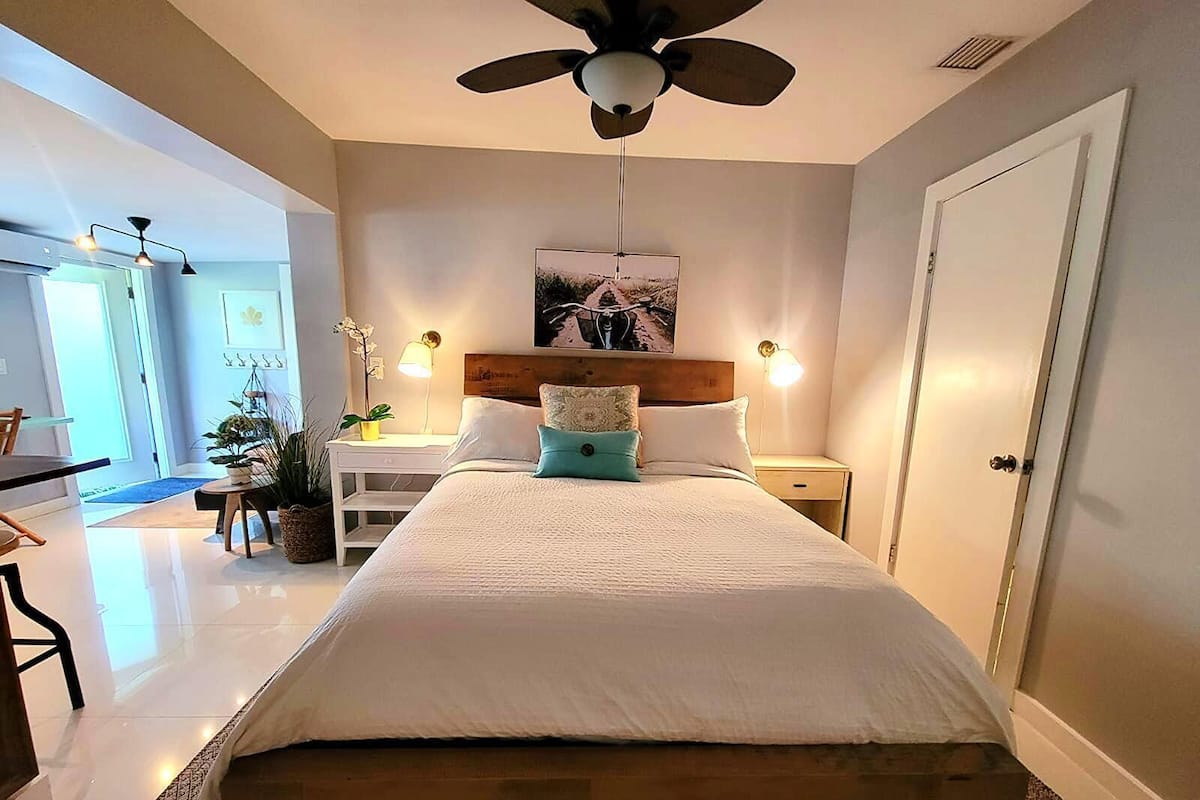 A bedroom with a bed, a ceiling fan, a nightstand, a lamp, and a door.