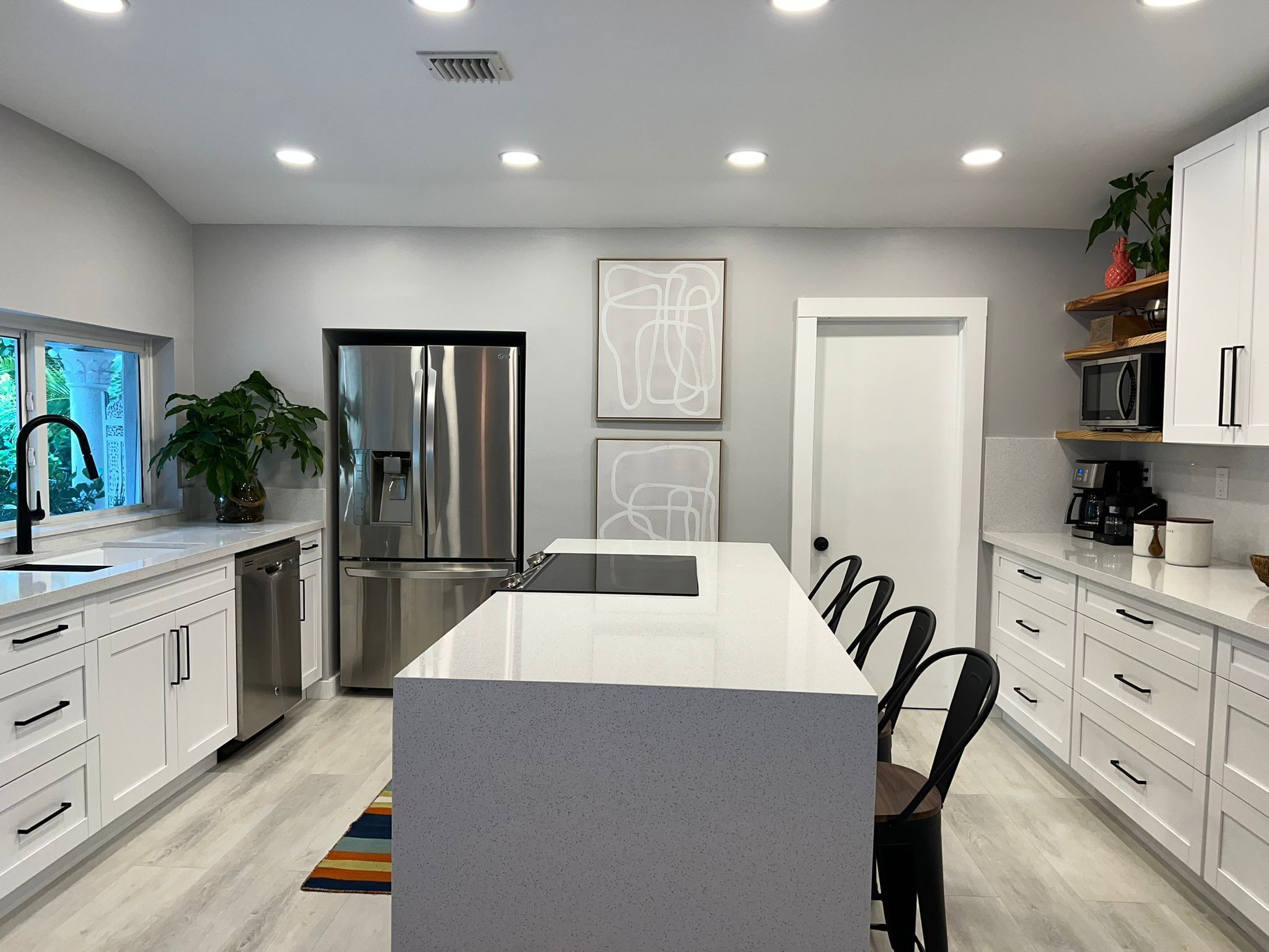 A modern kitchen with white cabinetry, a stainless steel refrigerator, a built-in oven, and a large island with a grey countertop.