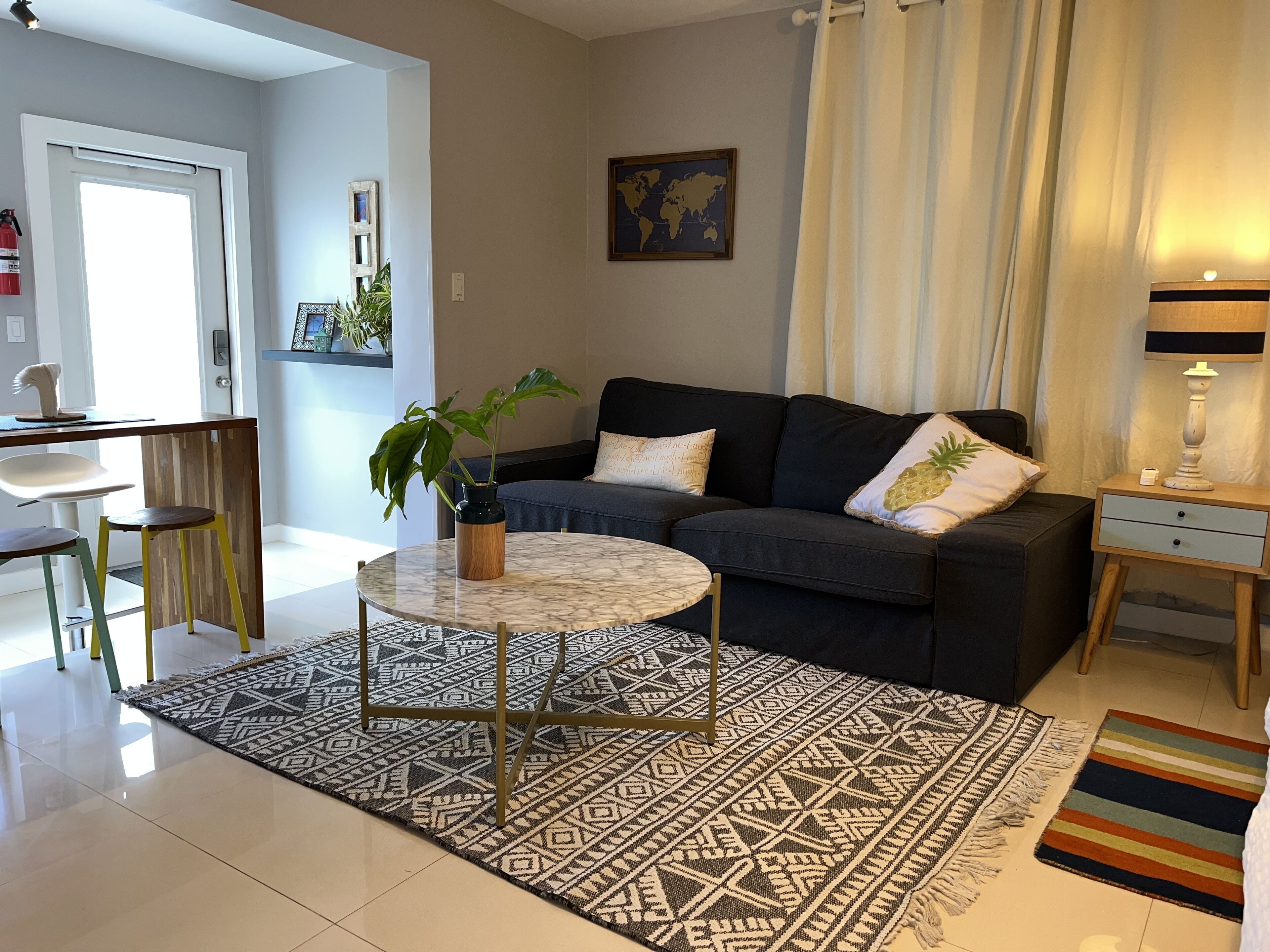 Ein modernes Wohnzimmer mit einem dunklen Sofa, einem runden Couchtisch, einem gemusterten Teppich und einem kleinen Beistelltisch mit Lampe.
