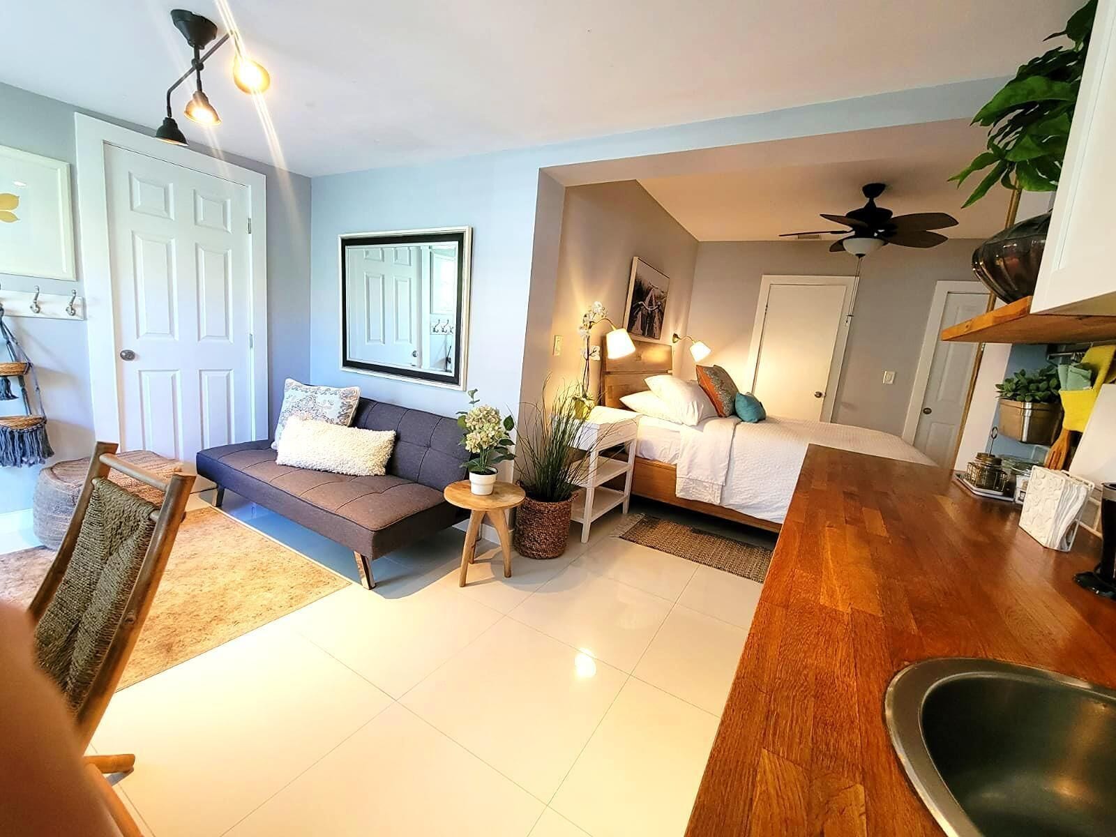 Un salon moderne avec un canapé, une petite table et un lit. On y trouve également un ventilateur de plafond et une plante dans un coin.