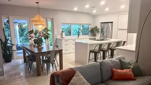 A modern kitchen with a central island, dining area with chairs, and a sofa with cushions.